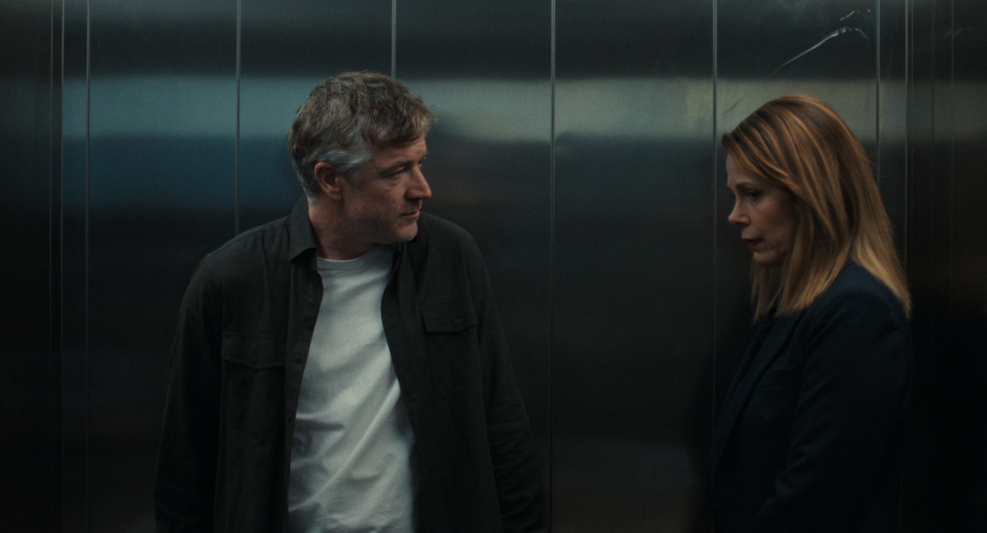 Still from Ungrateful Beings — two figures facing each other in a dim elevator