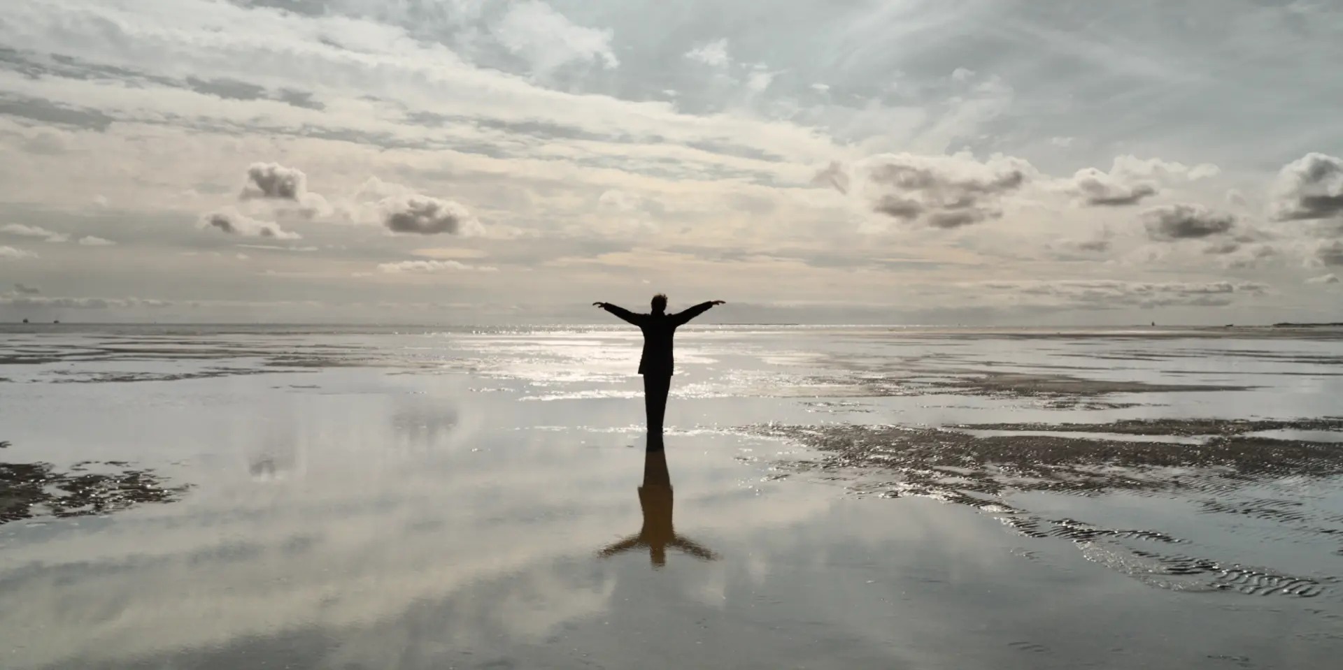 Still from Return to a Strange Land — two figures holding a cloth by the sea at sunset